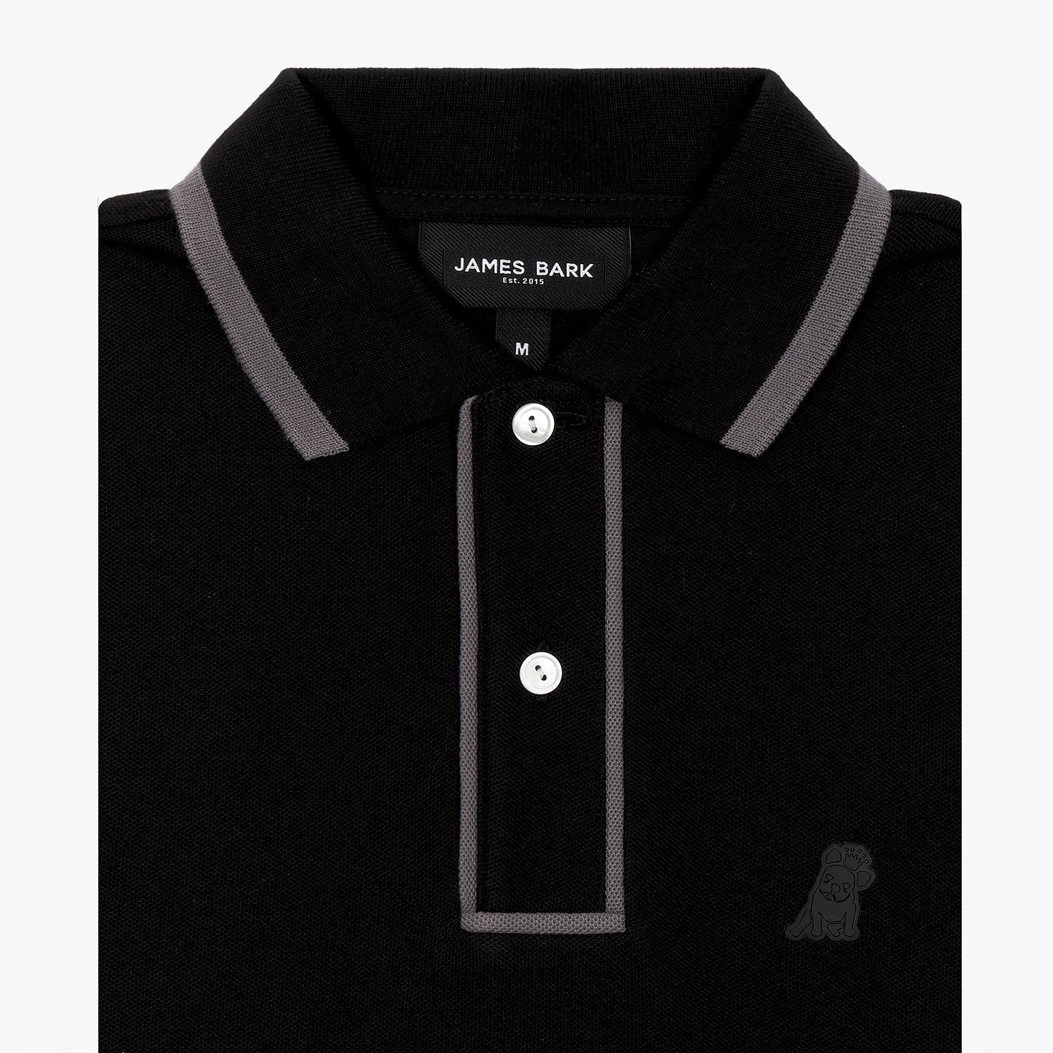 A close-up of a black polo shirt with contrasting gray trim on the collar and placket. The placket features two white buttons, and the brand label "James Bark Est. 2015" is visible inside the collar. The fabric has a textured finish, and an embossed dog logo is subtly placed on the left chest, blending into the black fabric.