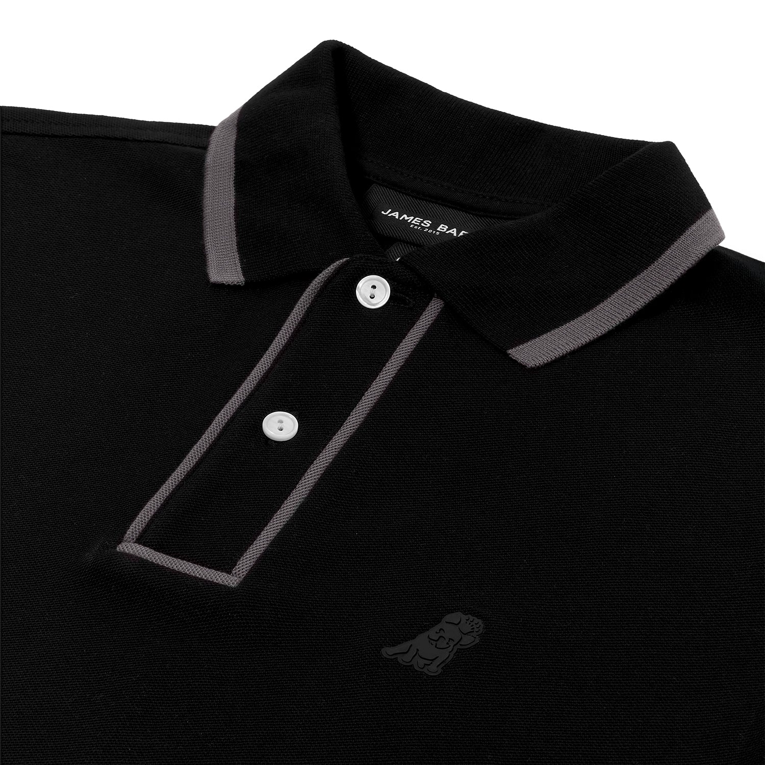 A close-up of a black polo shirt featuring gray trim along the collar and placket. The placket has two white buttons, and the brand label "James Bark Est. 2015" is visible inside the collar. The shirt’s textured fabric is accompanied by a subtle embossed dog logo on the left chest, blending into the black fabric.