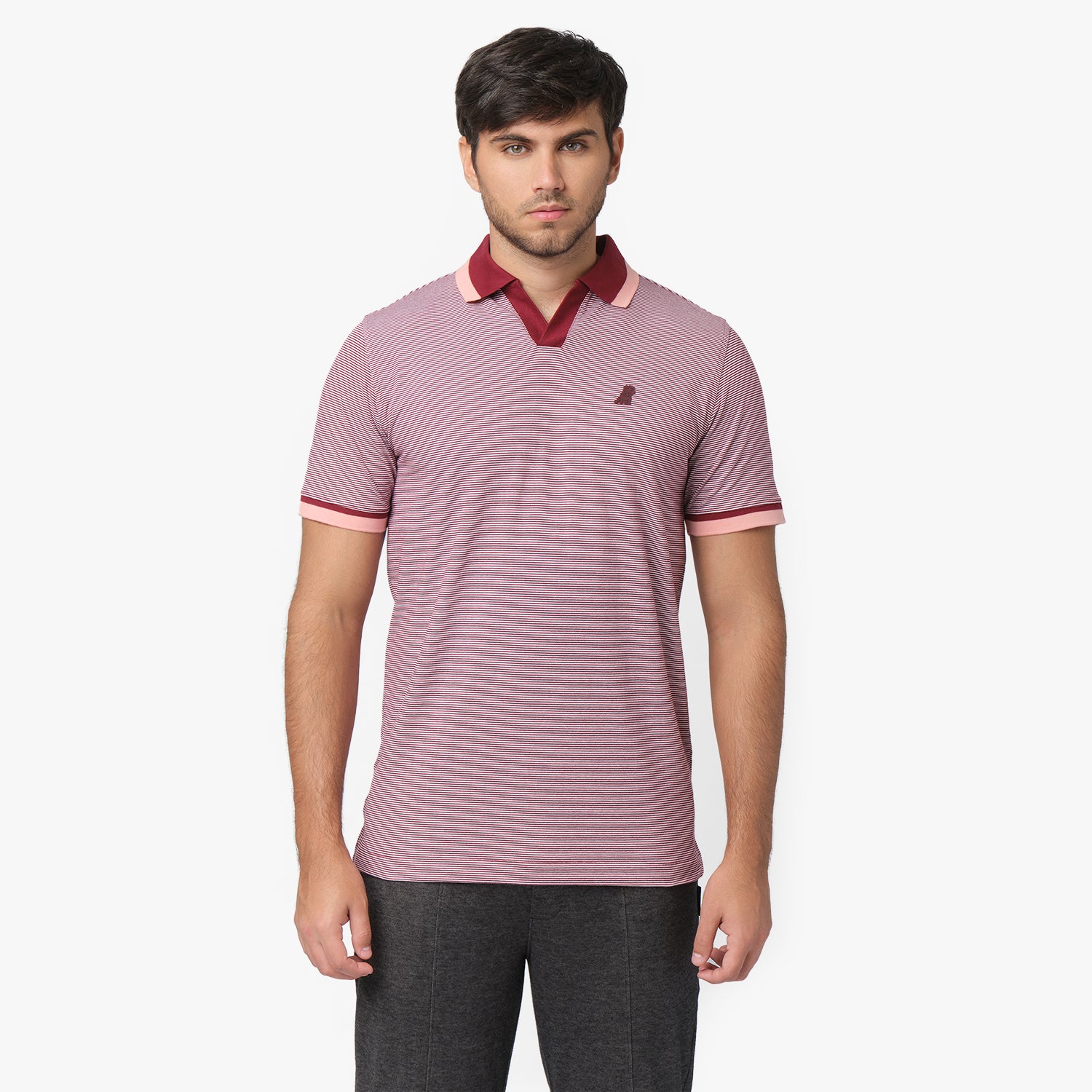 A male model wearing a fitted short-sleeve polo shirt with a fine red and white stripe pattern. The collar and sleeve cuffs feature contrasting burgundy and light pink accents. A small embroidered logo is visible on the left chest. The model pairs the polo with dark gray trousers and stands against a plain white background with a neutral expression