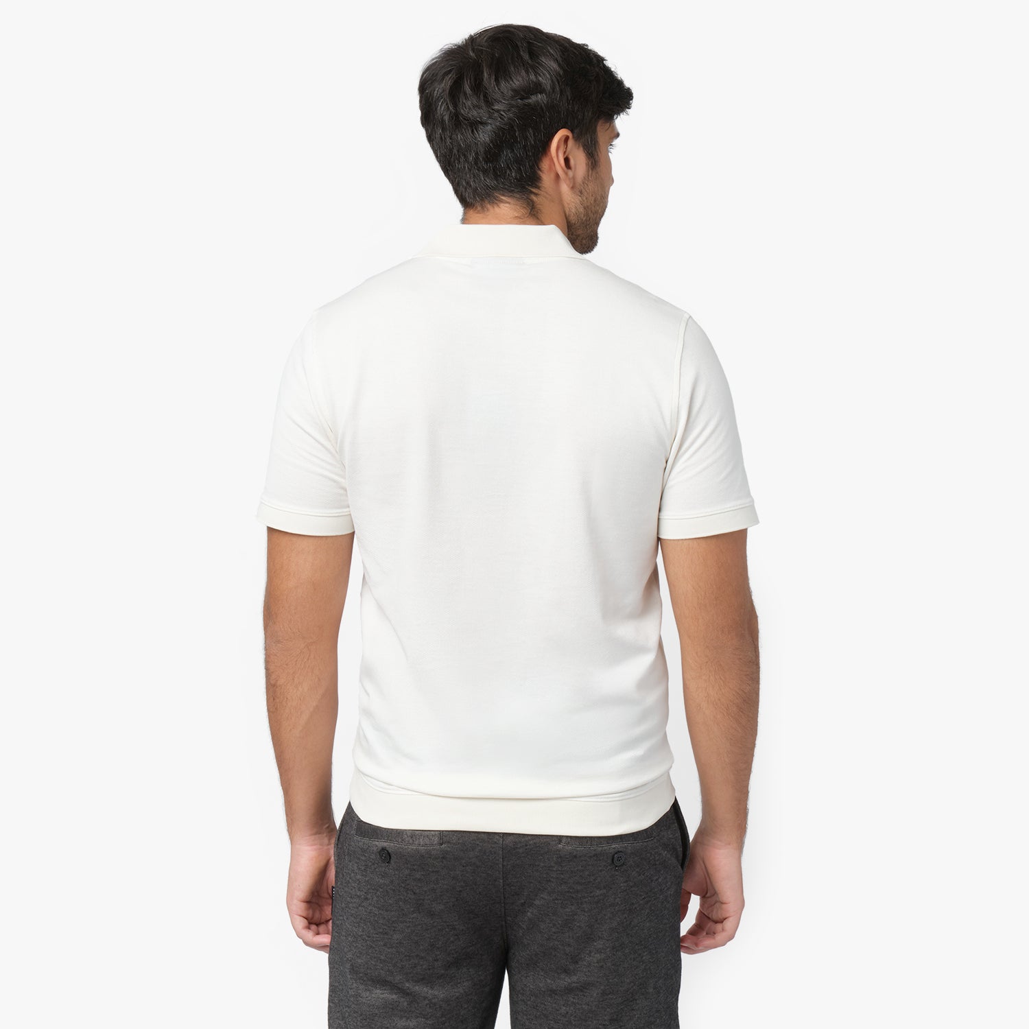 Rear view of a male model wearing a white short-sleeve polo shirt. The polo features a classic collar, ribbed sleeve cuffs, and a smooth, fitted design. Paired with dark gray trousers for a modern and casual look