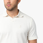 Close-up of a male model wearing a white short-sleeve polo shirt. The polo features a V-neck collar, ribbed sleeve cuffs, and a small embroidered dog logo on the chest, blending subtly with the fabric