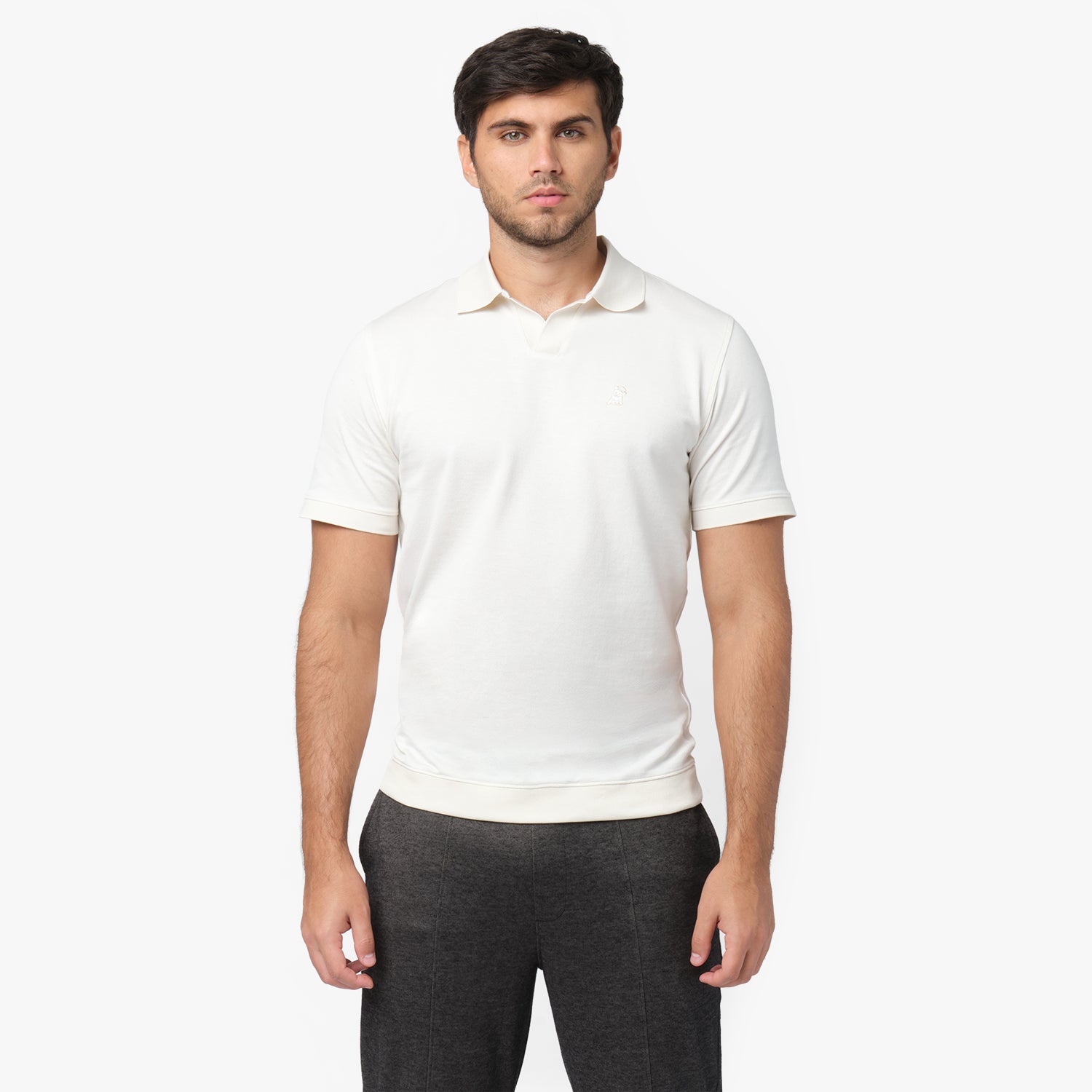 Male model wearing a white short-sleeve polo shirt with a minimalist design. The polo features a V-neck collar, ribbed sleeve cuffs, and a subtle embroidered logo on the chest. Paired with dark gray trousers for a casual yet refined look.