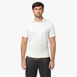 Male model wearing a white short-sleeve polo shirt with a minimalist design. The polo features a V-neck collar, ribbed sleeve cuffs, and a subtle embroidered logo on the chest. Paired with dark gray trousers for a casual yet refined look.