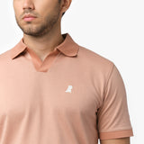 Close-up of a male model wearing a peach-colored short-sleeve polo shirt. The polo features a V-neck collar, ribbed sleeve cuffs, and a small embroidered white dog logo on the chest, adding a subtle design detail.