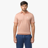 Male model wearing a peach-colored short-sleeve polo shirt with a V-neck collar, ribbed sleeve cuffs, and a small embroidered white dog logo on the chest. Paired with blue drawstring trousers for a stylish and casual look