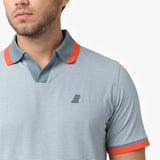 Close-up of a man wearing a light blue striped polo shirt with contrasting orange collar and sleeve trims. A small embroidered dog logo is visible on the left chest. The textured fabric and details of the collar are clearly shown. The background is plain white.