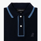 A navy blue polo shirt with a contrasting light blue trim on the collar and placket. The shirt features a two-button closure and an embroidered logo of a small dog on the lower right side. The brand label "JAMES BARK" is visible on the inside of the collar, indicating the size as "M". The fabric appears textured, resembling a classic pique material.