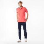 Full body picture of a man wearing a coral polo shirt and navy pants on a white background