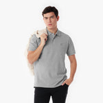 Man wearing a gray polo shirt holding a beige jacket on a white background