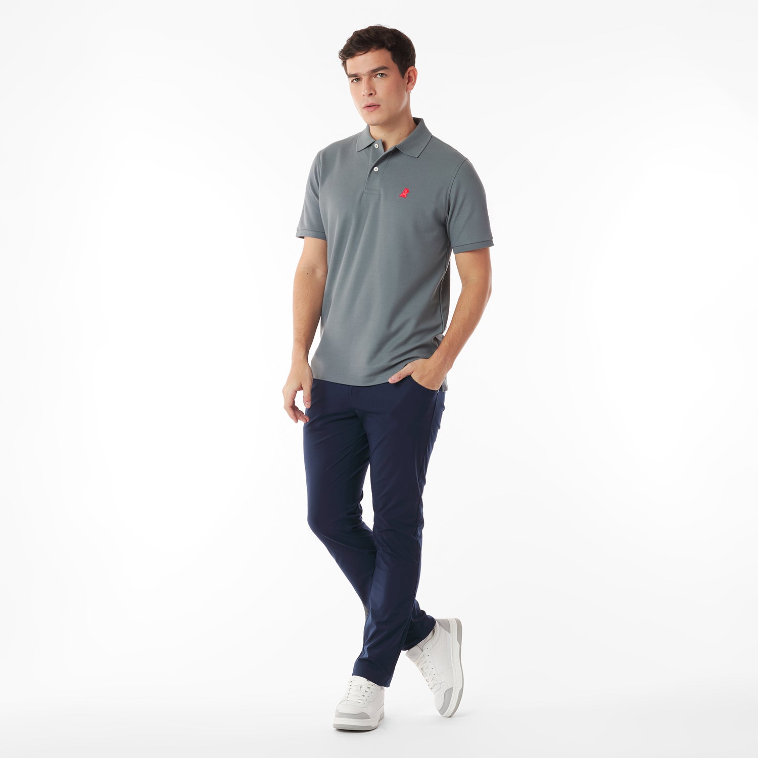 Full body picture of a man wearing a gray polo shirt with a red logo and navy pants on a white background