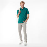 Full body picture of a man wearing a green polo shirt and light gray pants, holding a white bag on a white background