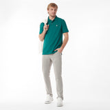 Full body picture of a man wearing a green polo shirt and light gray pants, holding a white bag on a white background