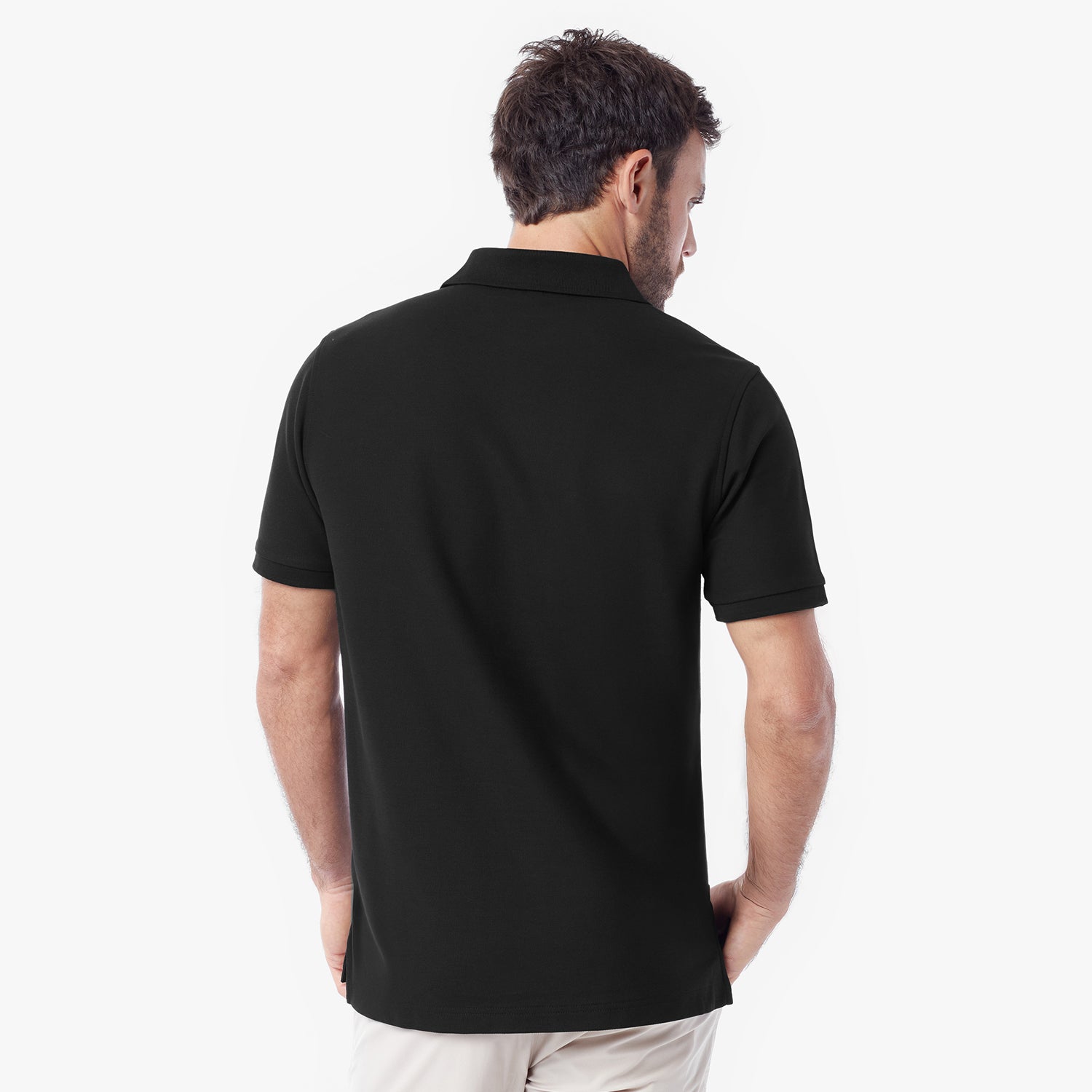A man viewed from the back wearing a black short-sleeve polo shirt and light beige pants