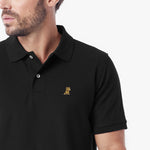 A close-up of a man wearing a black short-sleeve polo shirt with a small gold embroidered lion logo on the left chest
