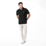 A man modeling a black short-sleeve polo shirt with a small embroidered logo on the chest, paired with light beige trousers