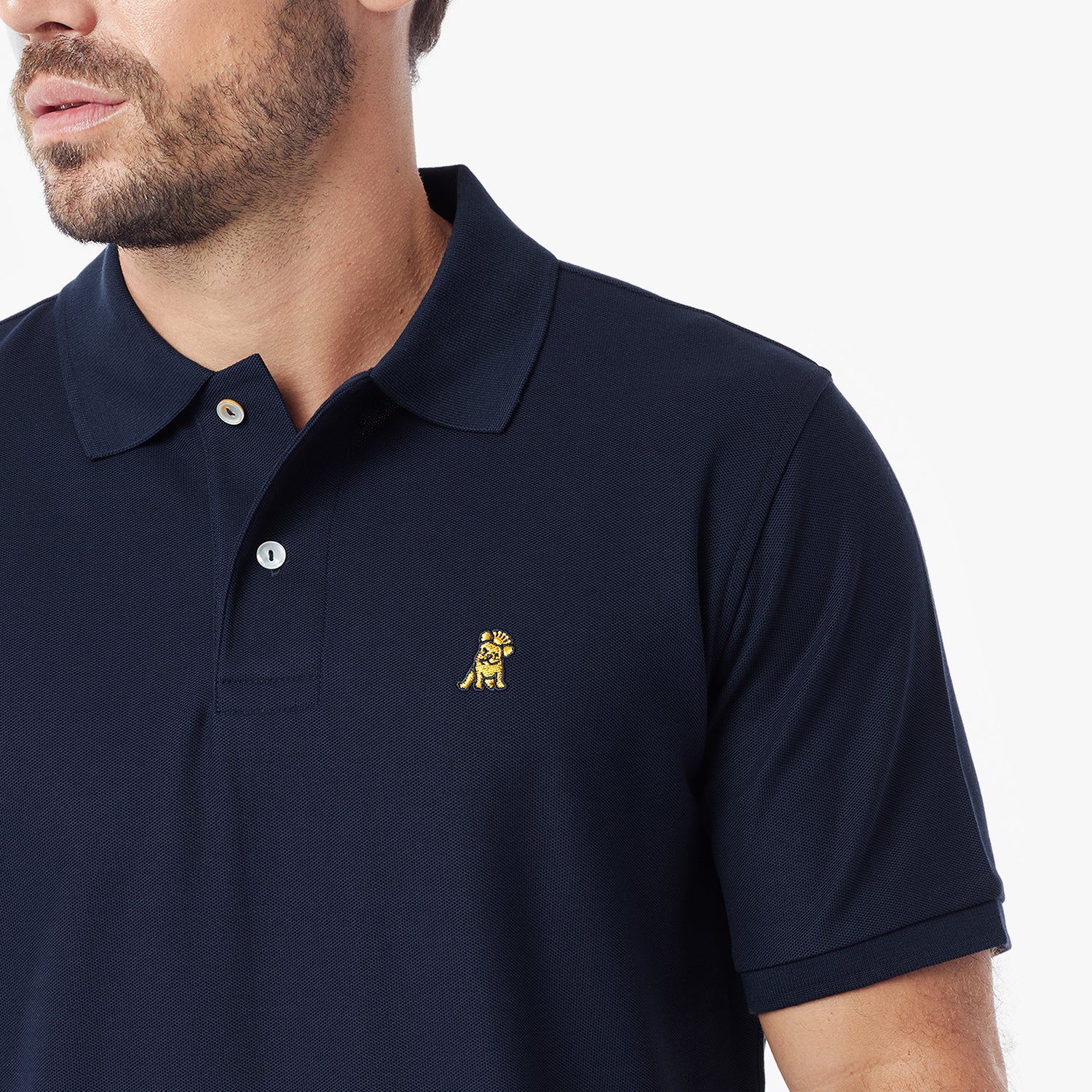 A close-up of a man wearing a navy blue polo shirt with a small embroidered dog logo on the left chest