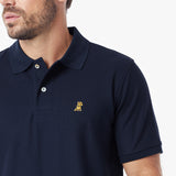 A close-up of a man wearing a navy blue polo shirt with a small embroidered dog logo on the left chest