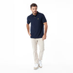 A man modeling a navy blue polo shirt with a small gold embroidered logo on the chest, paired with beige trousers