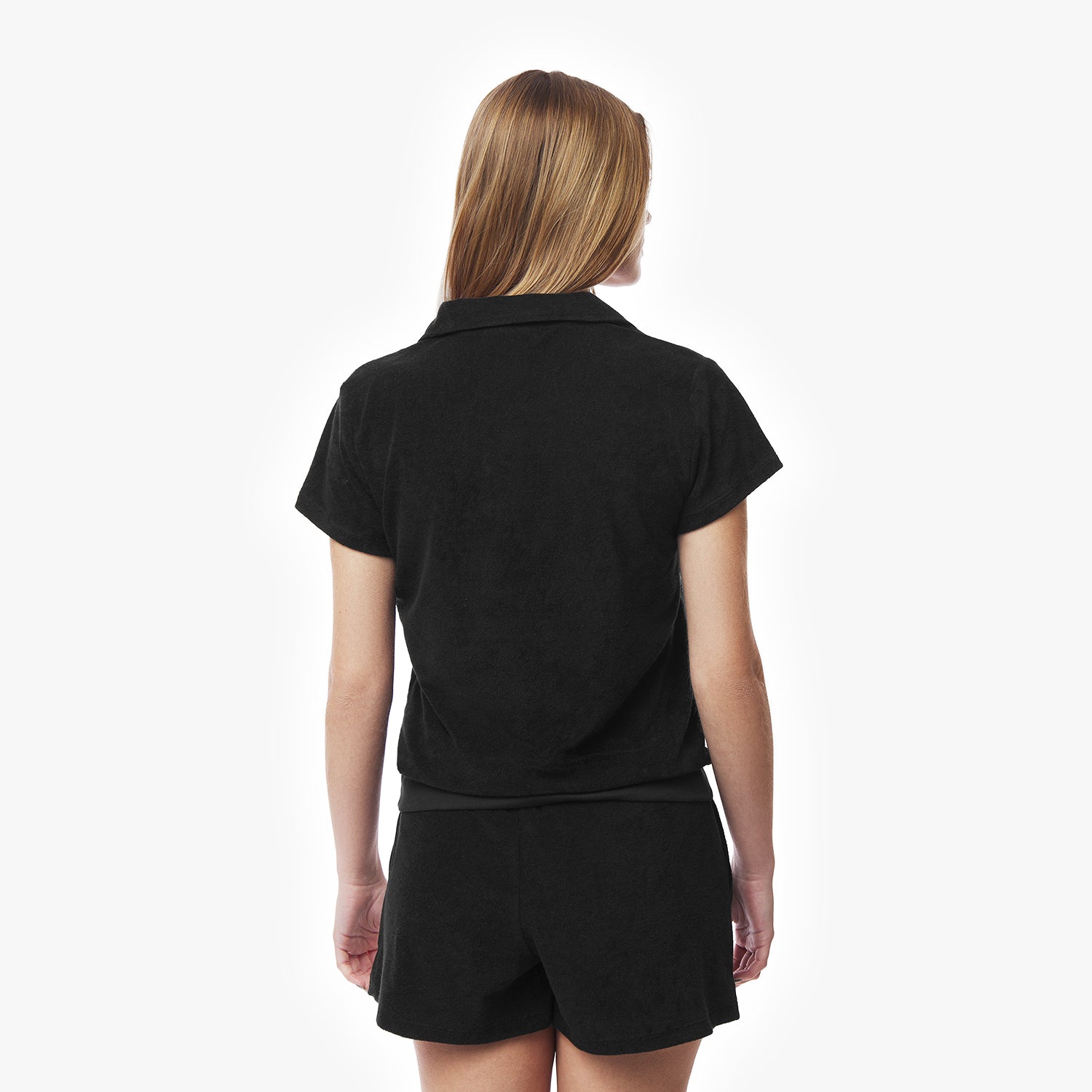 Rear view of a woman wearing a black collared shirt and black shorts, highlighting the back design of the shirt