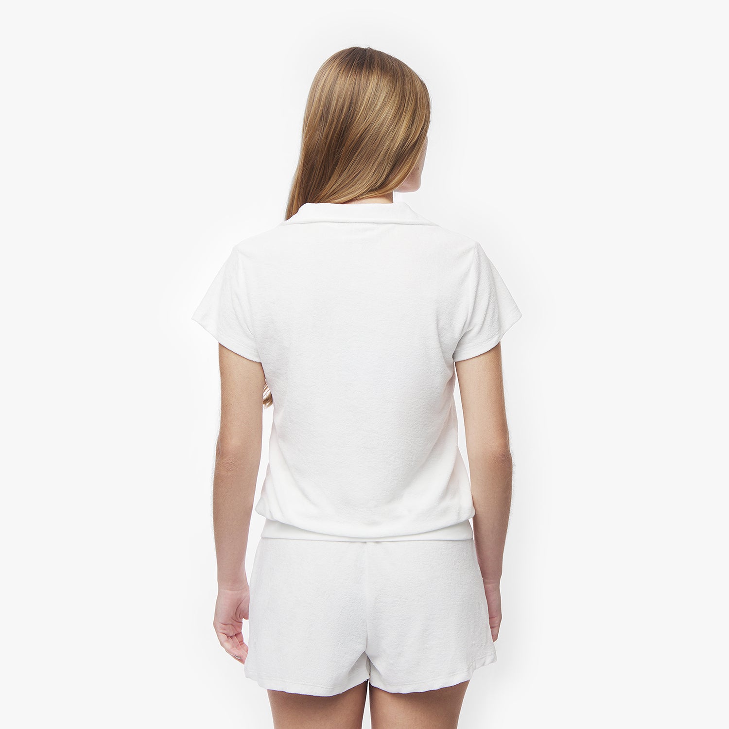 Rear view of a woman wearing a white collared shirt and white shorts, showcasing the back design of the shirt