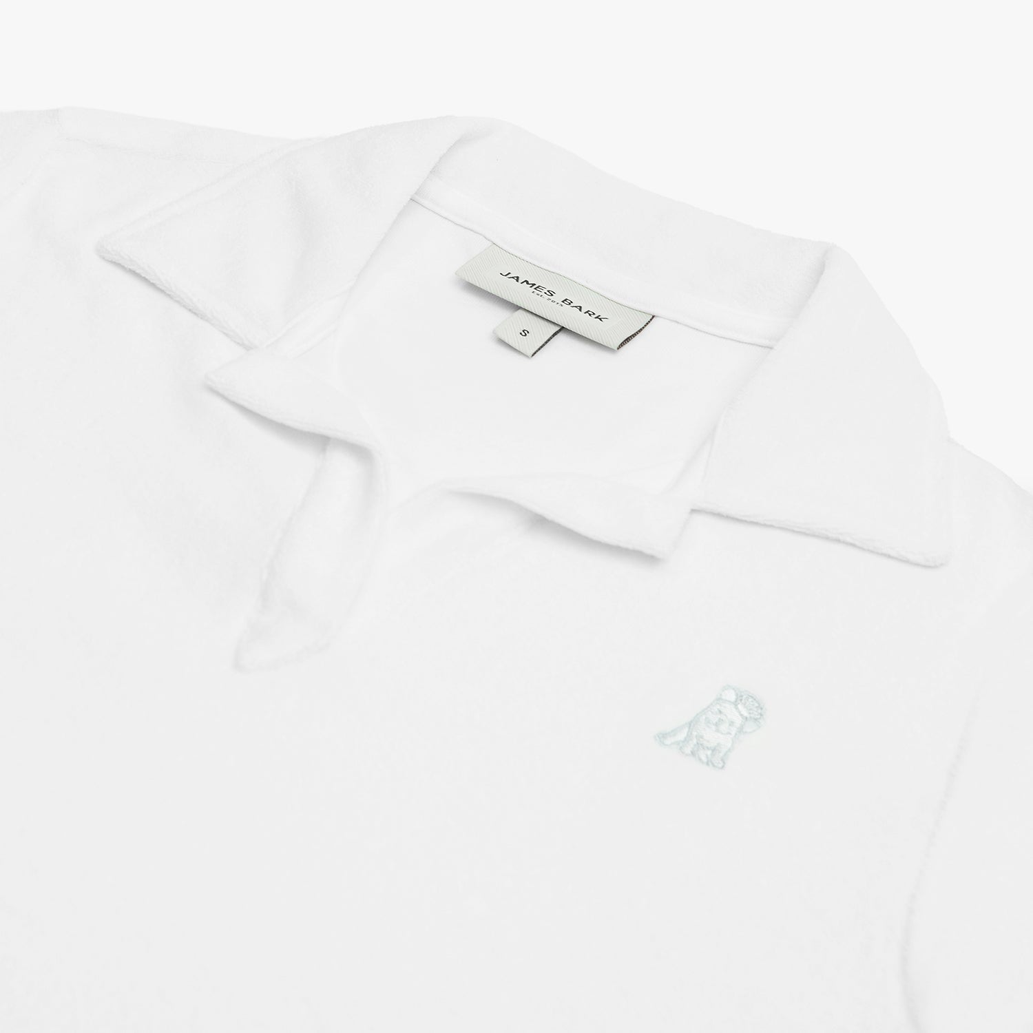 Detail view of the white collared shirt's neckline and embroidered logo near the chest area