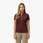 Woman models a maroon short-sleeve polo shirt with white buttons and small embroidered logo, paired with beige trousers. Front view against white background