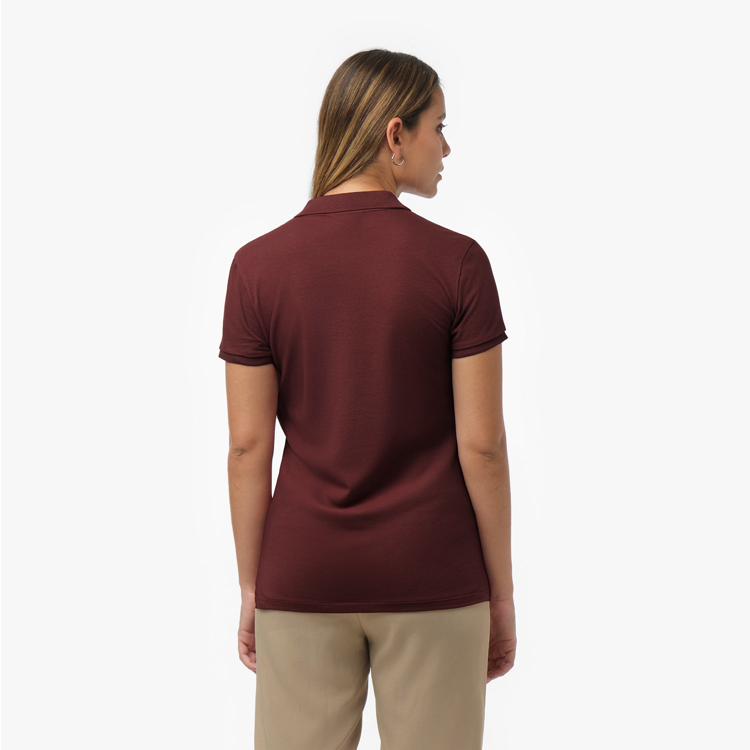 Back view of a woman wearing a short-sleeved maroon polo shirt and beige trousers against a white background