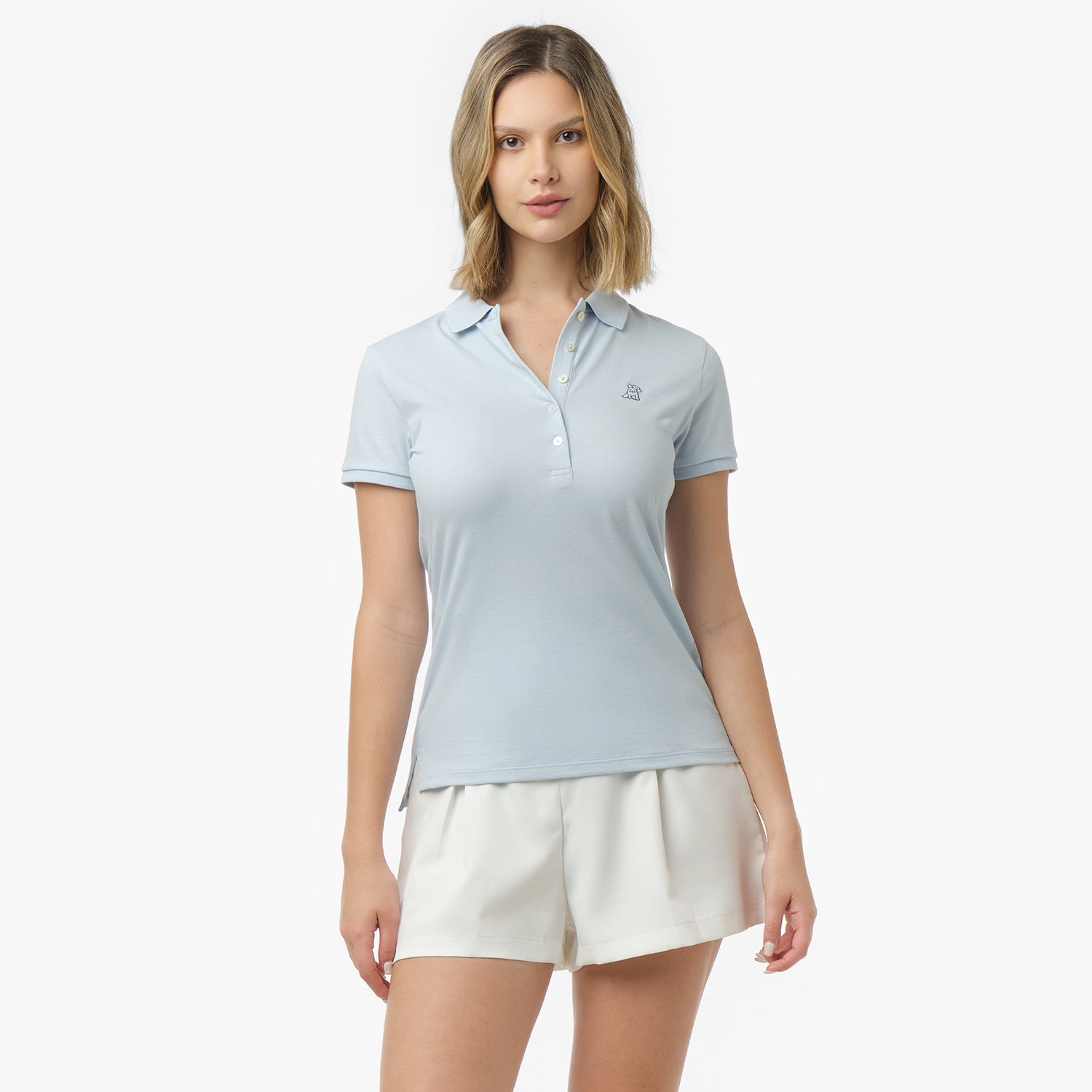 Woman models a light blue short-sleeve polo shirt with white buttons and small embroidered logo, paired with white shorts. Front view against white background