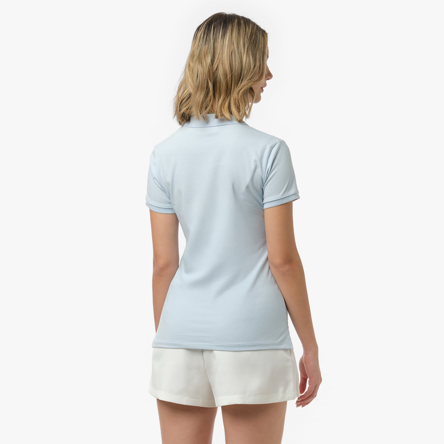 Back view of a woman wearing a short-sleeved light blue polo shirt and white shorts against a white background