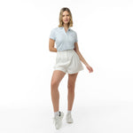 Full-length view of a woman modeling a light blue polo shirt, high-waisted white shorts, white socks, and white sneakers. Dynamic pose against white background