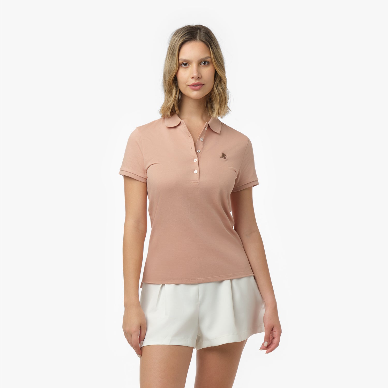 Woman models a peach short-sleeve polo shirt with white buttons and darker embroidered logo, paired with white shorts. Front view against white background