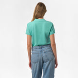 Rear view of a woman wearing the light turquoise polo shirt, showing the plain back design, paired with blue jeans.