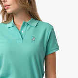 Close-up of the woman's chest area, highlighting the embroidered logo and button collar of the light turquoise polo shirt.