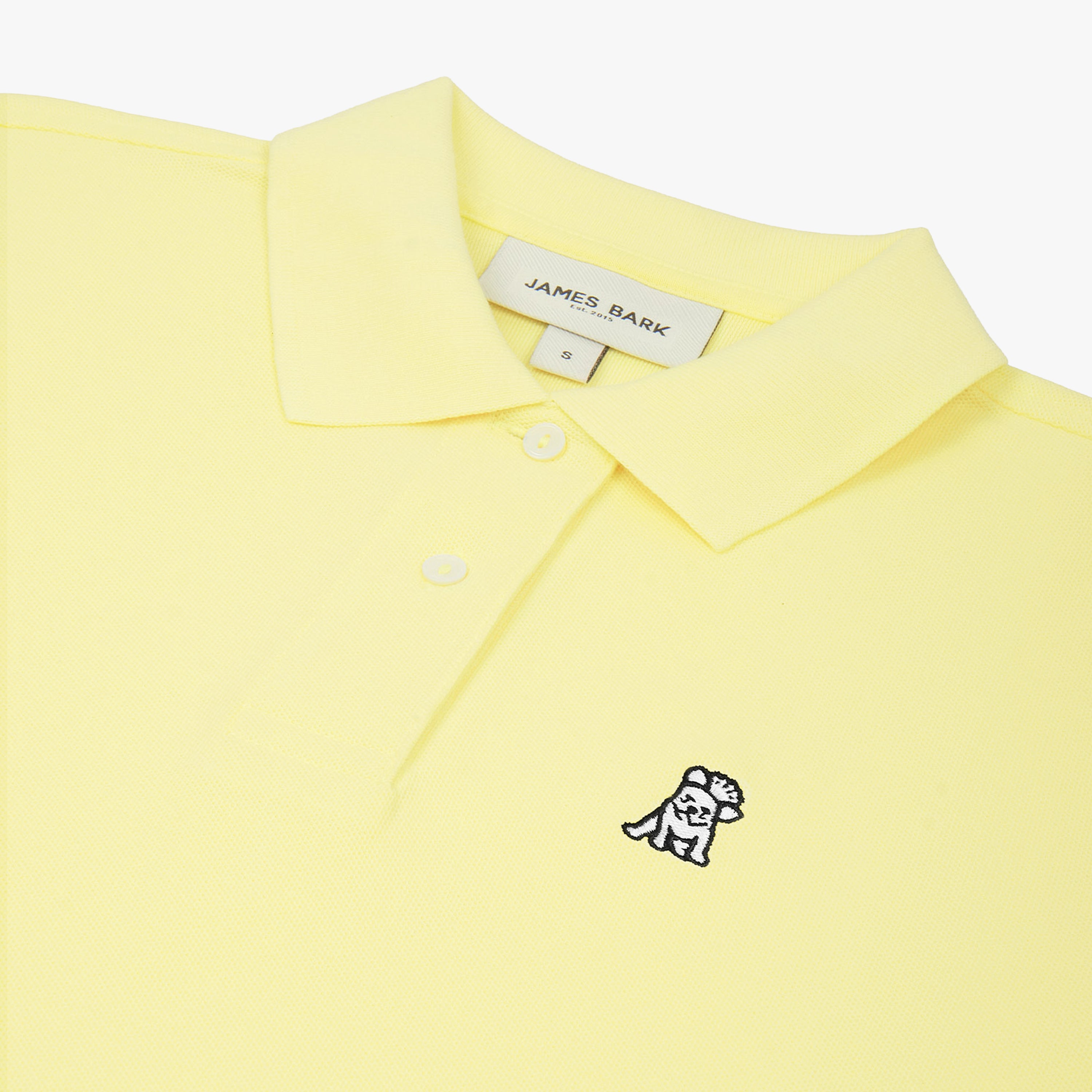 Close-up of the woman's chest area, highlighting the embroidered logo and button collar of the yellow polo shirt.