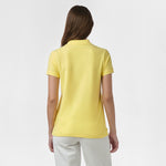 Rear view of a woman wearing the yellow polo shirt, showing the plain back design, paired with white pants