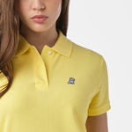 Close-up of the woman's chest area, highlighting the embroidered logo and button collar of the yellow polo shirt.