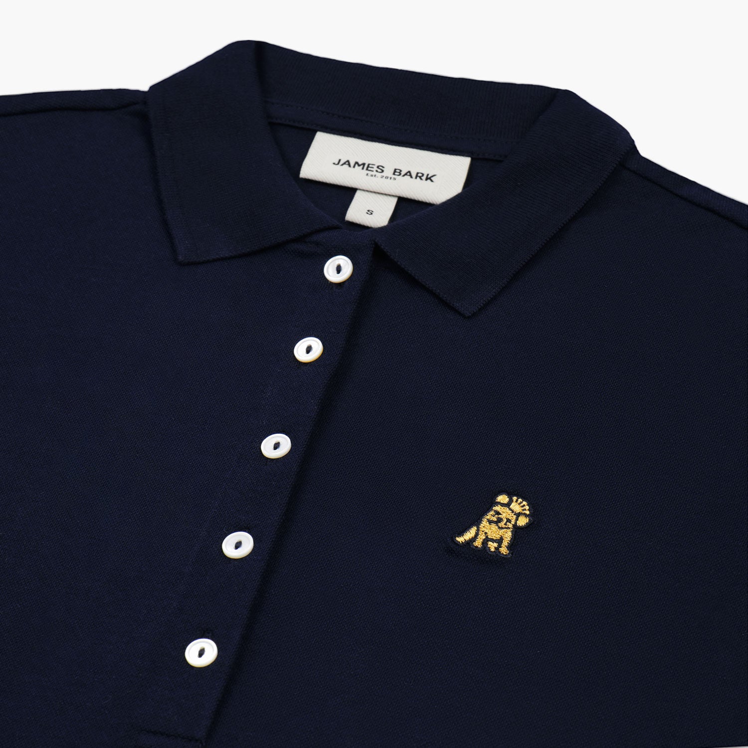 Close-up of the woman’s face and chest, highlighting the collar and gold logo on the navy blue polo shirt.