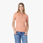 Woman wearing a peach polo shirt and blue jeans on a white background