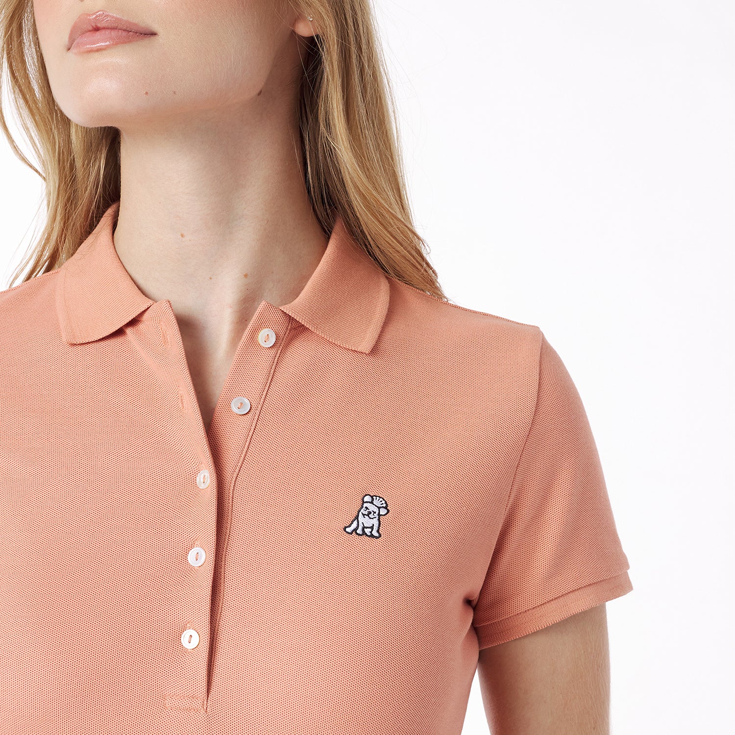 Close-up of a person wearing a pink polo shirt with a small logo on a white background