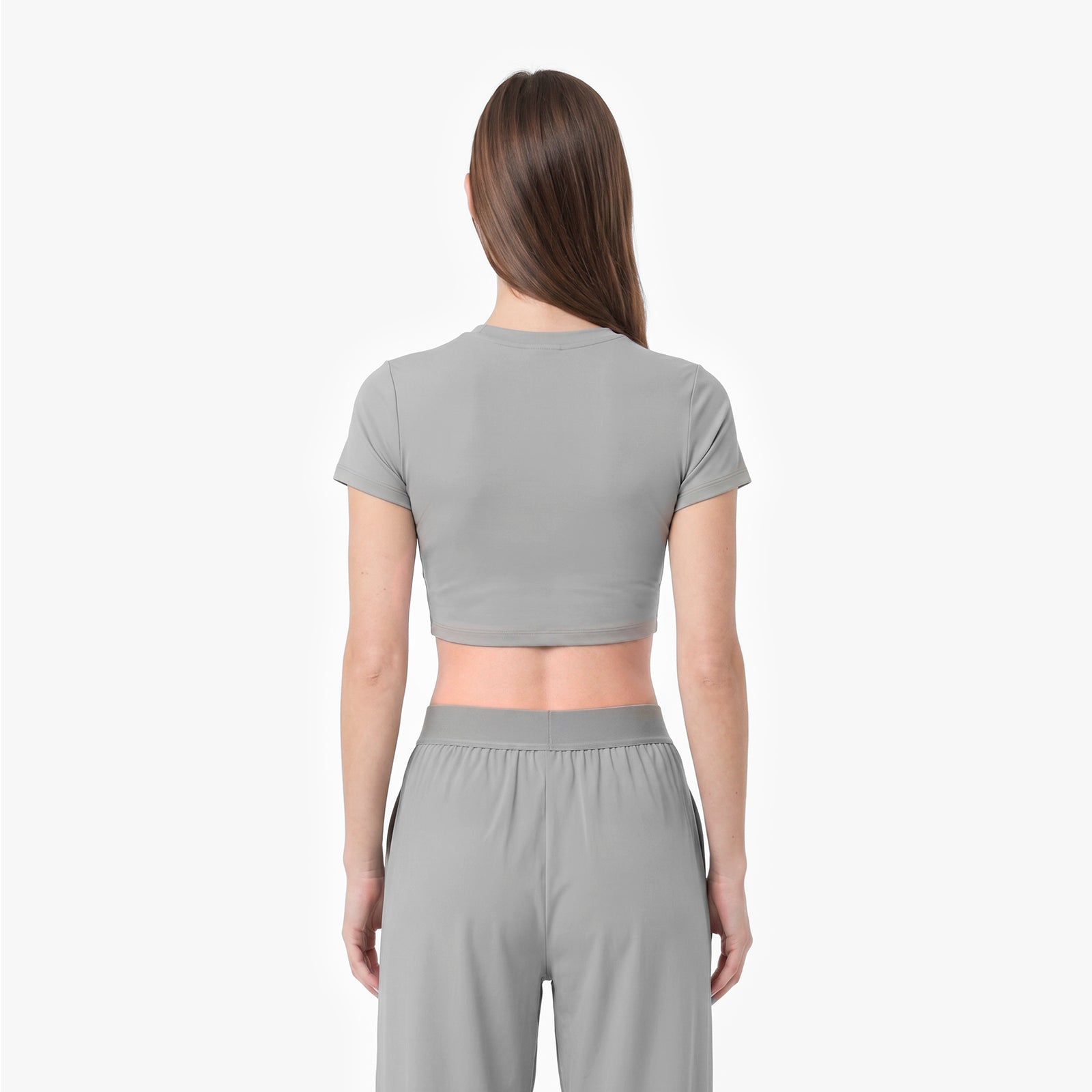 Woman wearing a gray crop top and pants on a white background