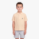 A young boy modeling a light peach-pink polo shirt with a small embroidered logo on the left chest