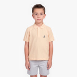 A young boy modeling a light peach-pink polo shirt with a small embroidered logo on the left chest