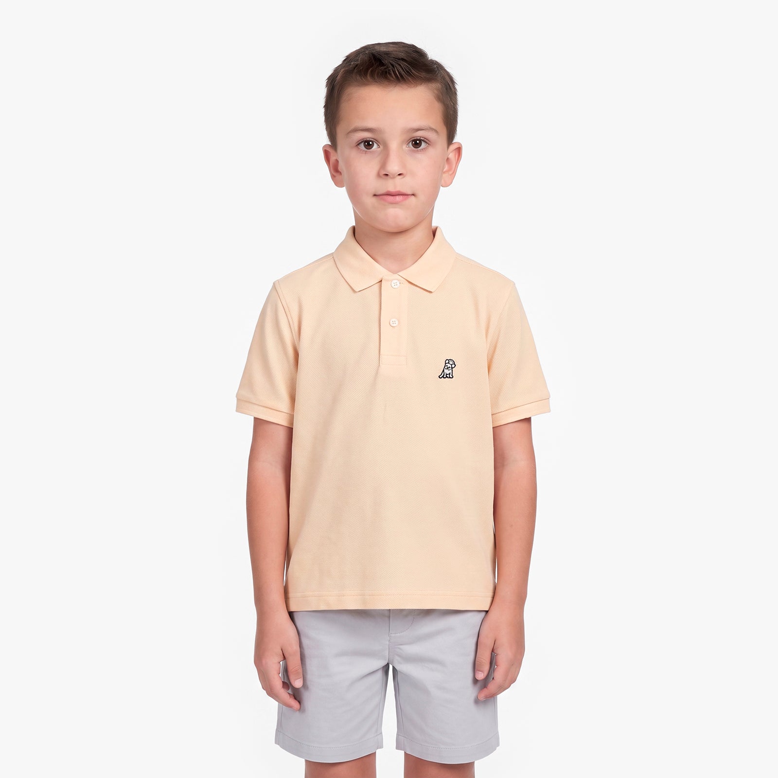 A young boy modeling a light peach-pink polo shirt with a small embroidered logo on the left chest