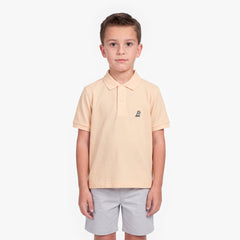 A young boy modeling a light peach-pink polo shirt with a small embroidered logo on the left chest