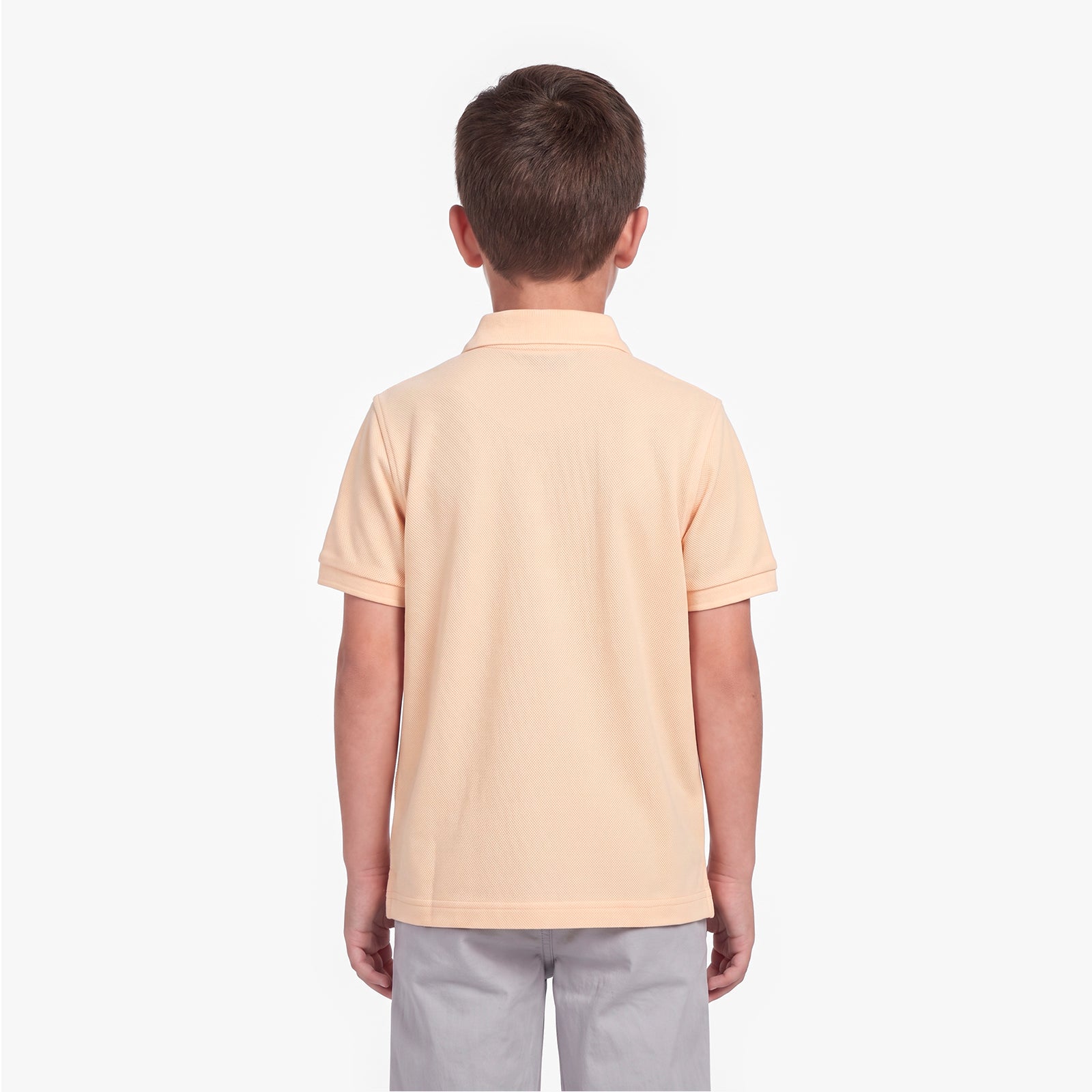 A child viewed from the back wearing a polo shirt in a pale peach-beige color