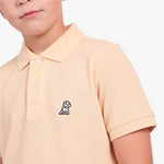 A close-up of a child wearing a light peach-pink polo shirt with a small embroidered dog logo on the chest