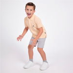Full body picture of a boy wearing a peach pink polo shirt with light gray shorts