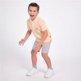 Full body picture of a boy wearing a peach pink polo shirt with light gray shorts