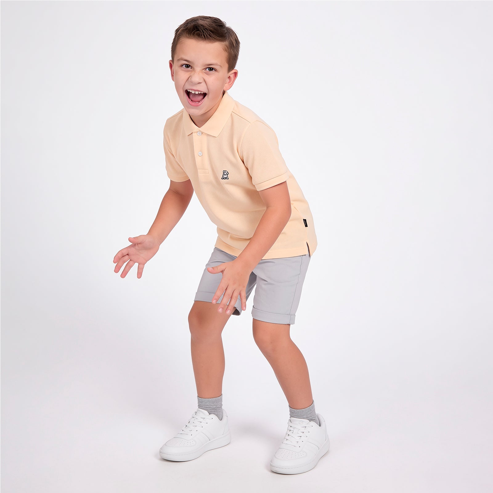 Full body picture of a boy wearing a peach pink polo shirt with light gray shorts