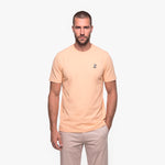 Man wearing a beige t-shirt with a small logo on a white background